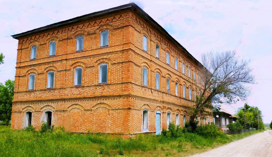 Dreigeschossiges Schulhaus aus rotem Backstein in Huck an der Wolga, daneben ein Holzhaus und ein Feldweg
